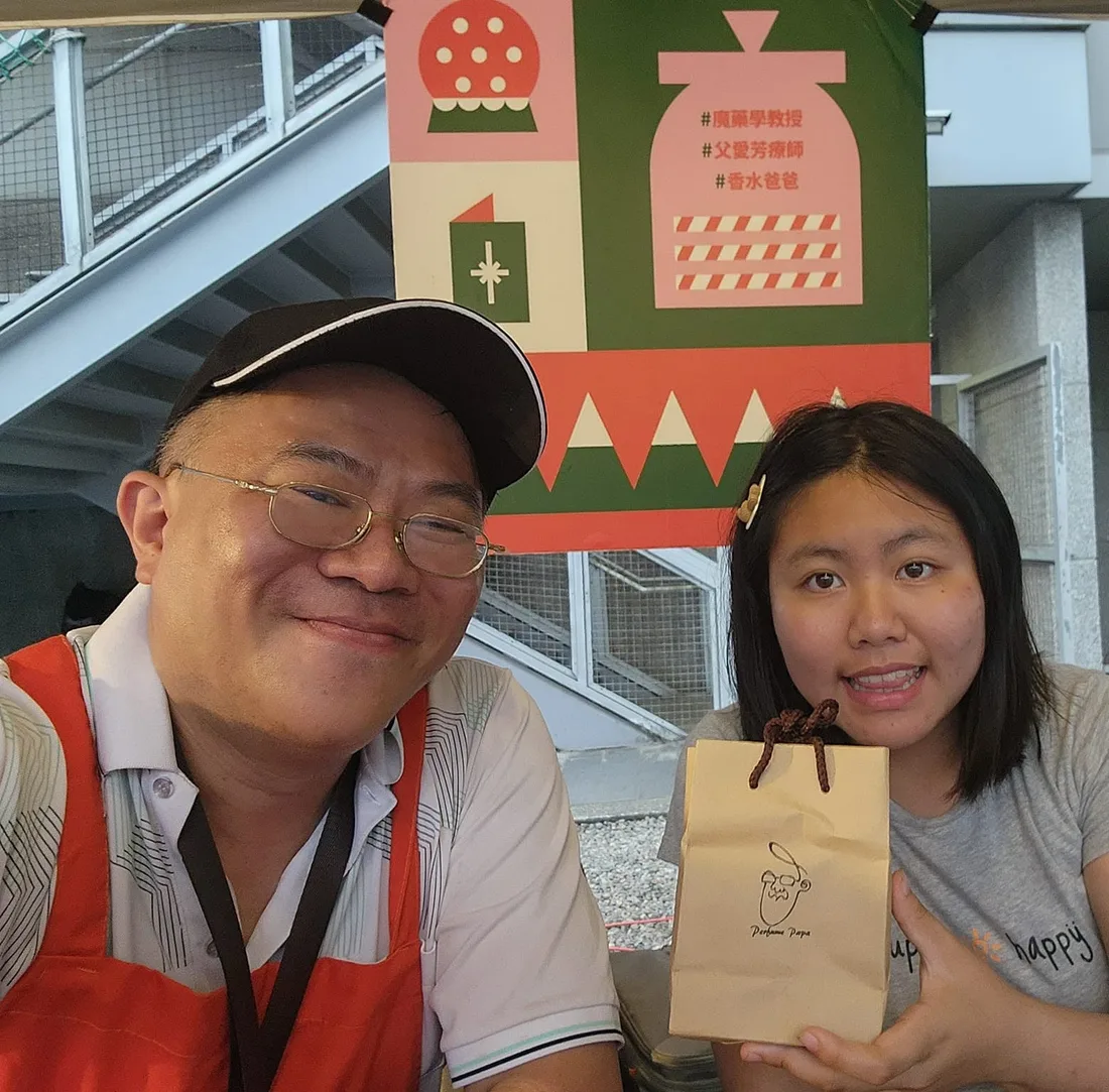 市集攤位上,香水爸爸與女兒拿著品牌紙袋合影